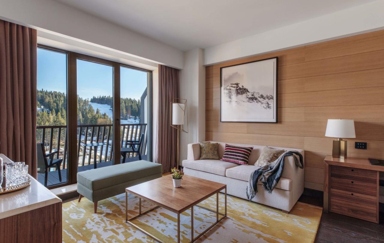 The living soace in a suite with a couch, desk, bench, and access to a balcony at Viceroy Kopaonik Serbia