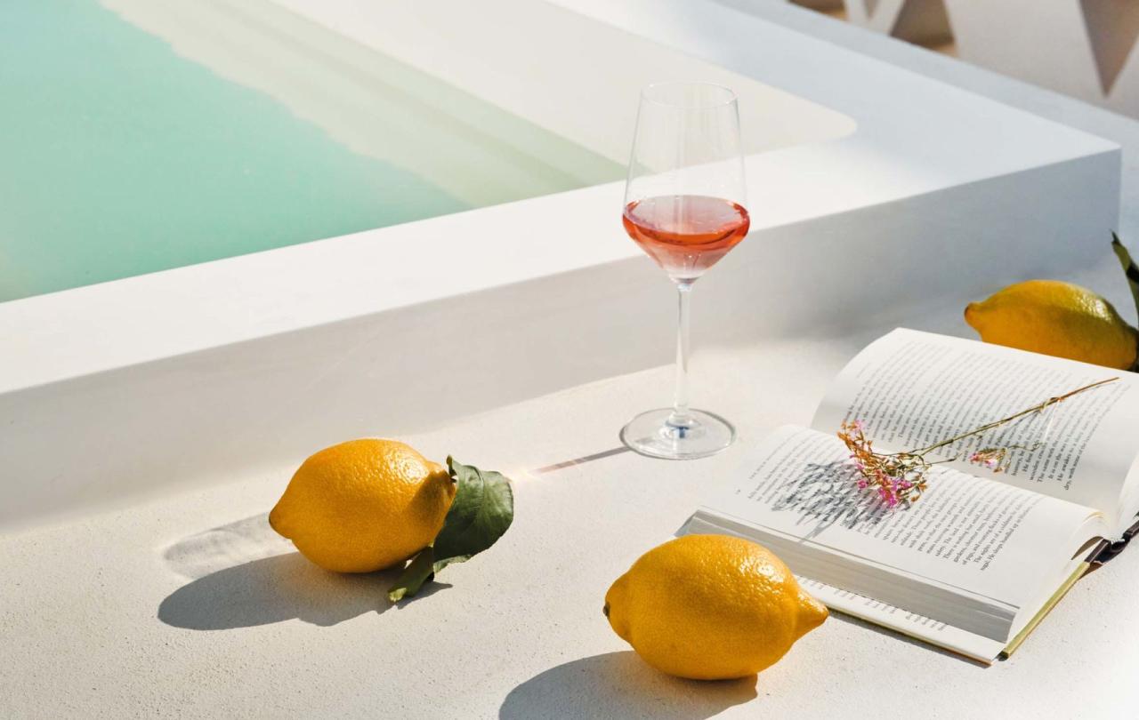 Lemons next to an open book and a glass of wine next to a pool