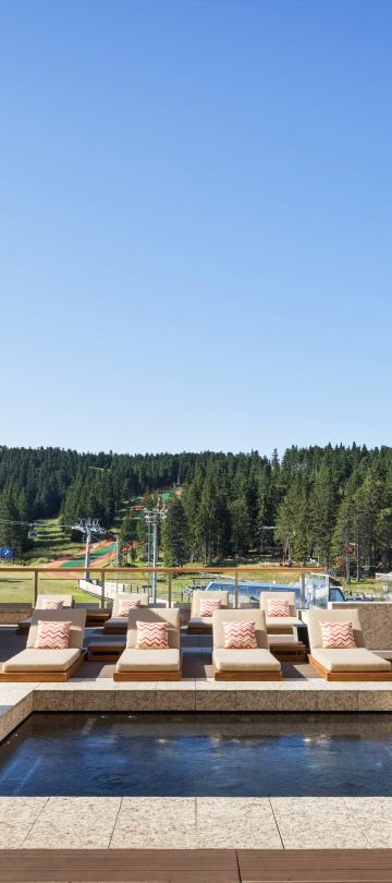 A whirlpool surrounded by pool cabanas, with rolling green tree-topped hills in the background