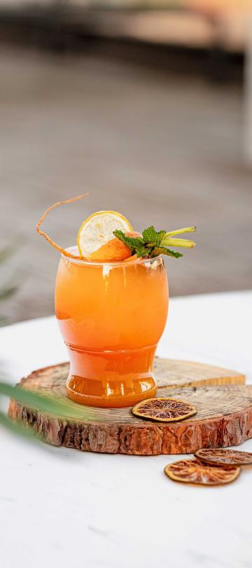 A bright orange citrus cocktail with a green garnish, served on a wood slab at Hush, the rooftop bar at Viceroy Washington DC