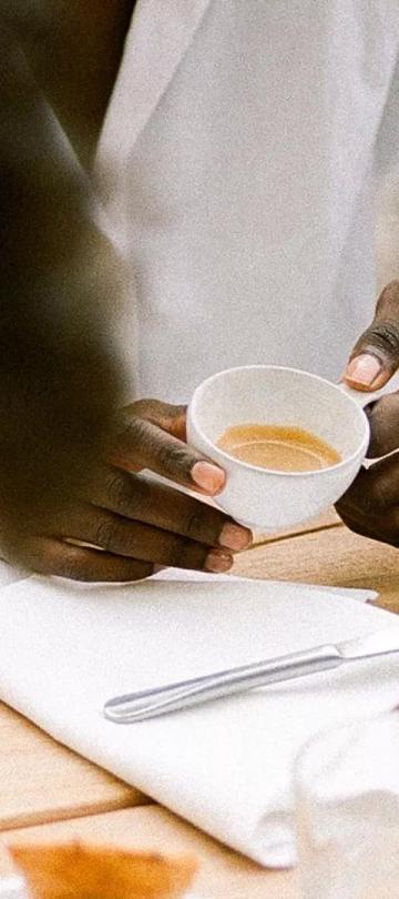 Detail of a pair of hands holding a coffee mug, with a plate of waffles on the table