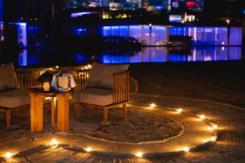A table set up for two people on the beach with lights in the sand, rose pedals, and a bottle of chilled champagne at Los Cabos