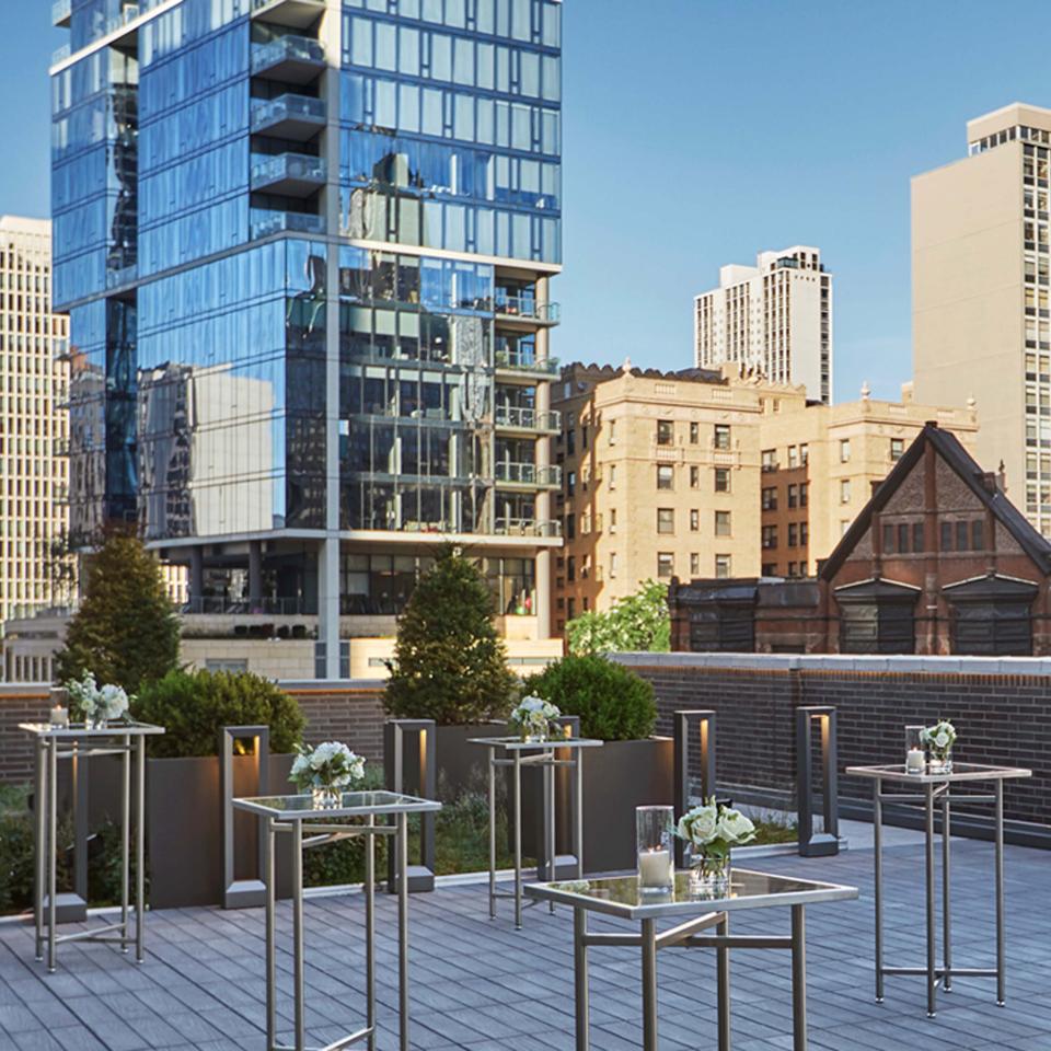 A terrace at Viceroy Chicago, looking out on the urban landscape, decorated with small glass tables