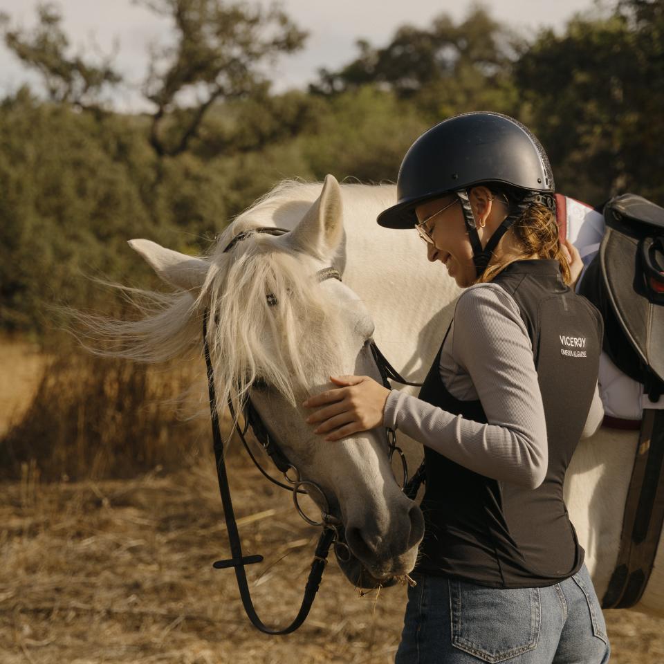 A woman in riding gear pets the nose of a white horse in the Algarve countryside