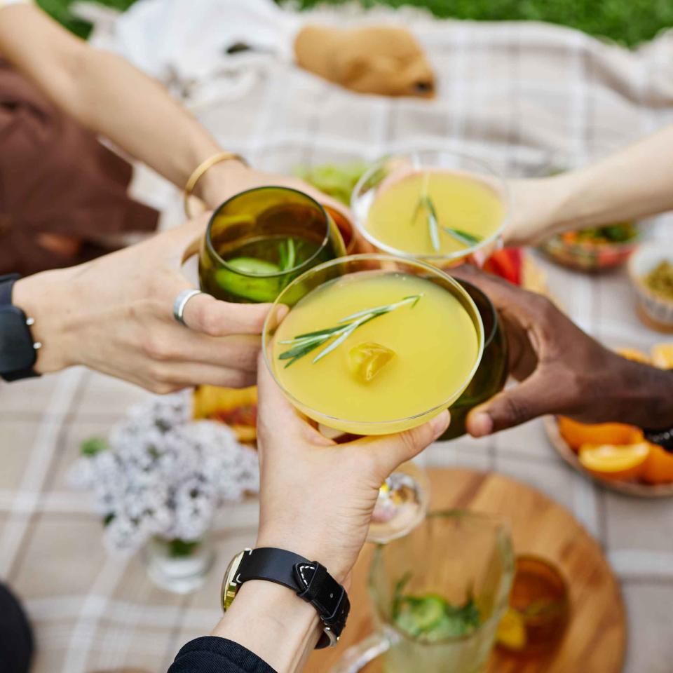 Three friends toasting their cocktails on a picnic blanket