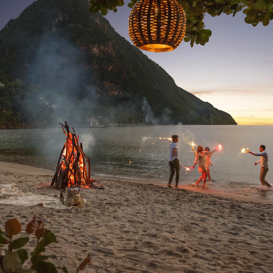 A family dances on the beach with sparklers at dusk.