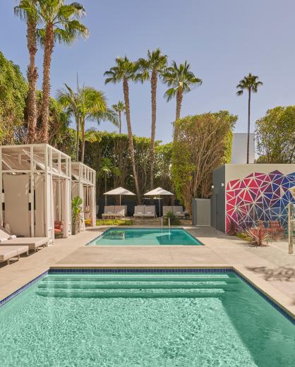 A palm-tree lined outdoor pool at Viceroy Santa Monica, surrounded by cabanas and a bar