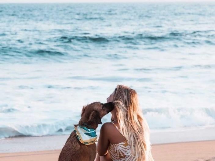 woman and dog sit on beach