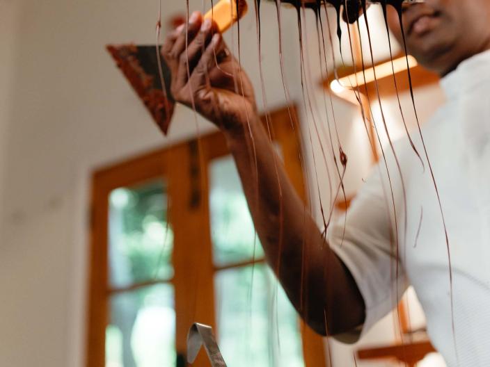 person holding a spatula and tray dripping with chocolate