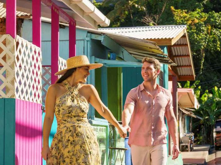 couple holding hands walk past bright coloured buildings