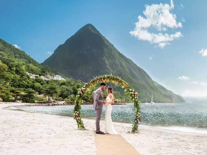 bride and groom stand under floral arch on beach